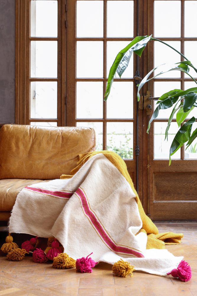 Plaid berbero bicolore bianco e giallo con pompon rosa in lana, realizzato a mano in Marocco.