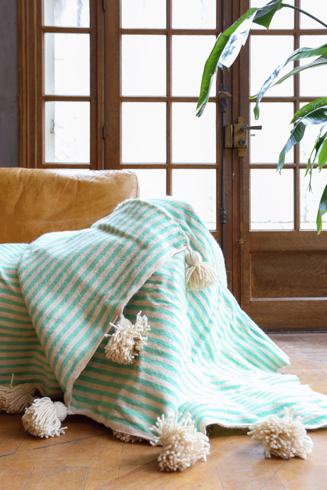 Handmade Moroccan Berber blanket with white pompoms and turquoise stripes made of wool.