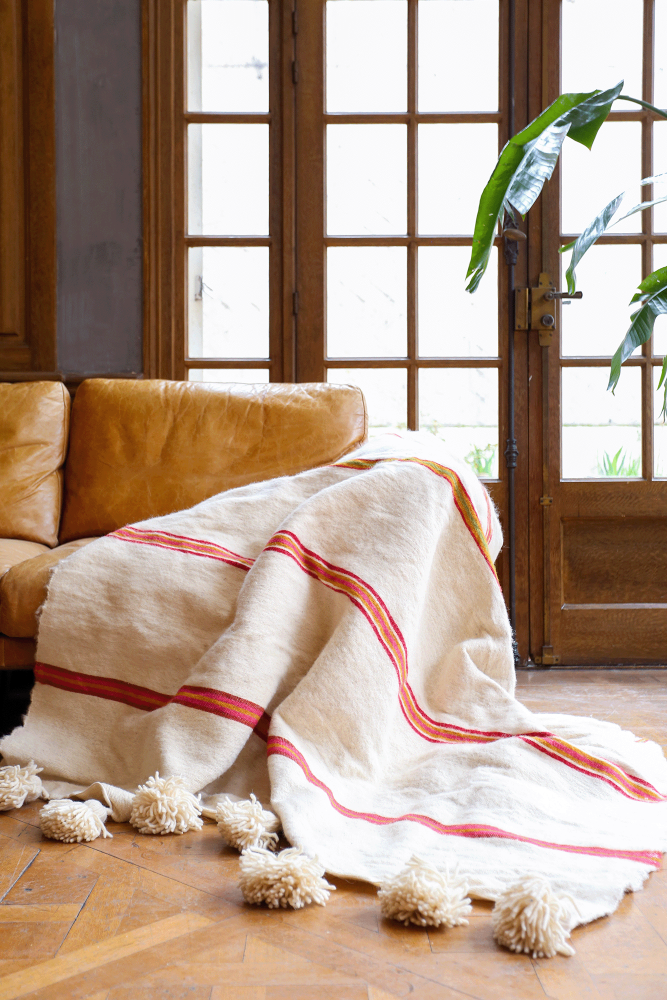 Handmade Moroccan wool blanket with white pompoms and pink stripes.